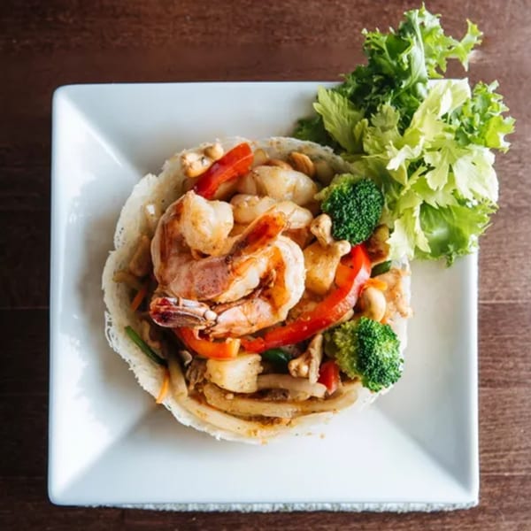 Thai stir-fried shrimp and vegetables in a crispy noodle bowl, garnished with fresh lettuce.