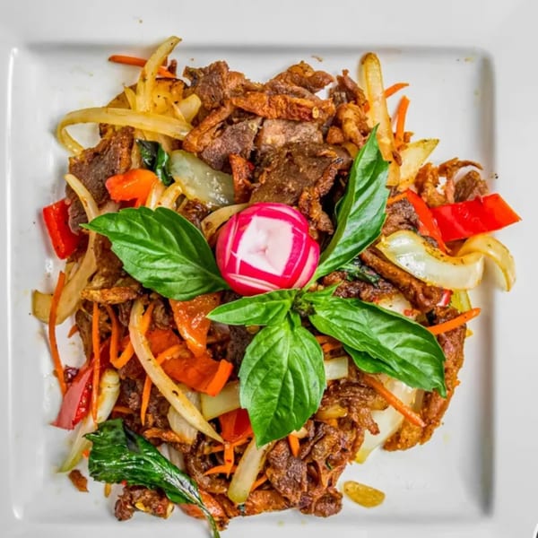 Thai crispy beef with onions, bell peppers, carrots, basil, and a radish garnish.