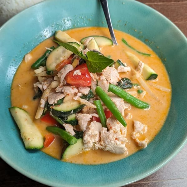 A vibrant Thai red curry with chicken, zucchini, green beans, and bamboo shoots in a blue bowl.