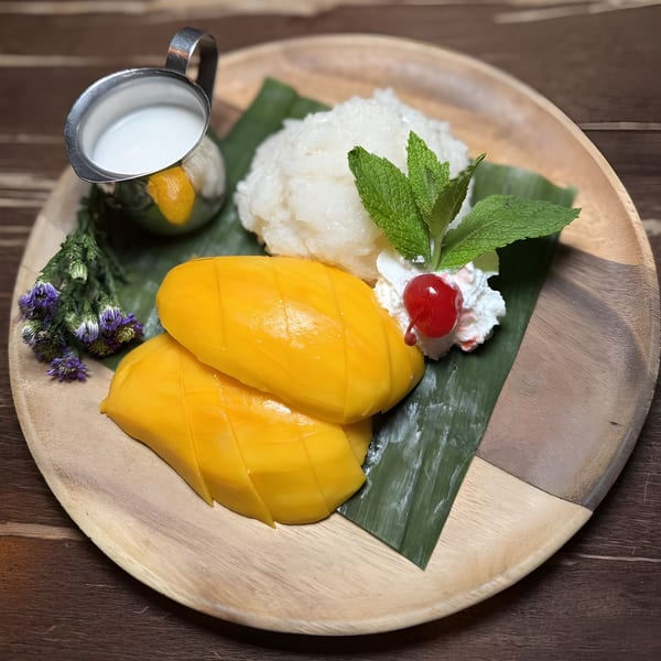 Mango sticky rice with coconut milk, mint, and a cherry on a wooden plate.