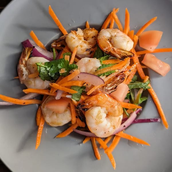Grilled shrimp with julienned carrots, red onion, and fresh herbs in a gray bowl.