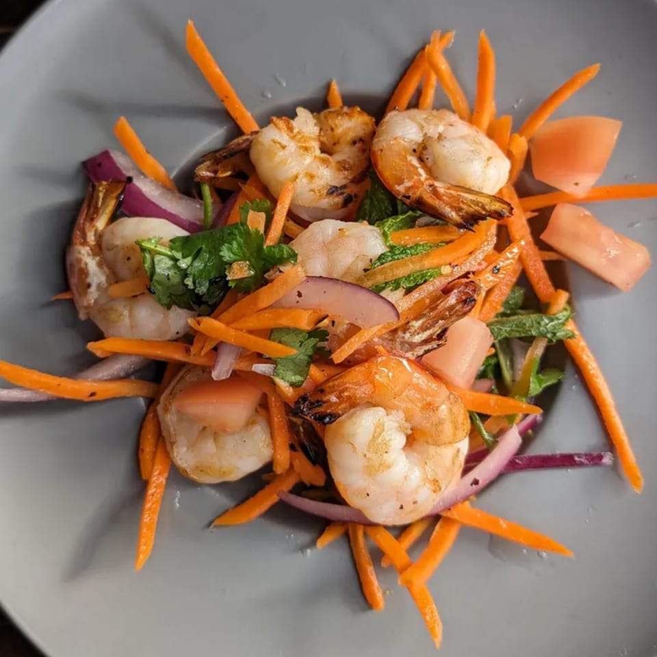 Grilled shrimp with julienned carrots, red onion, and fresh herbs in a gray bowl.