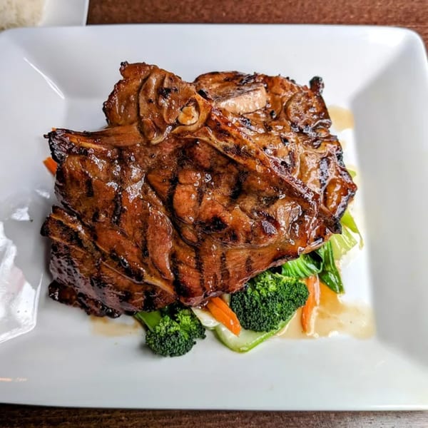 Grilled pork chop with broccoli, carrots, and bok choy on a white plate at Lantern Thai.