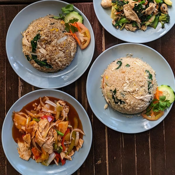 Four plates of Thai food, including fried rice and stir-fries, on a dark wooden table.